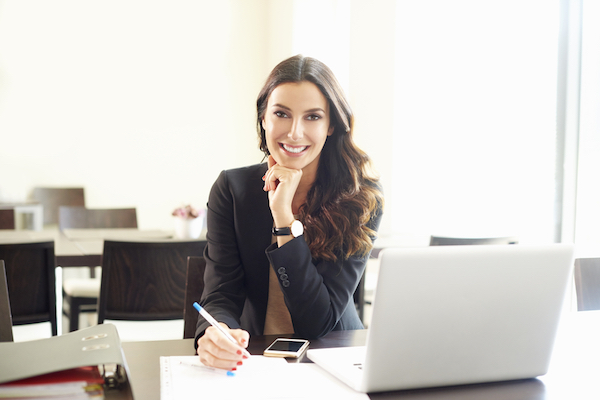 attractive brunette smiling at her laptop as she considers first marketing campaign