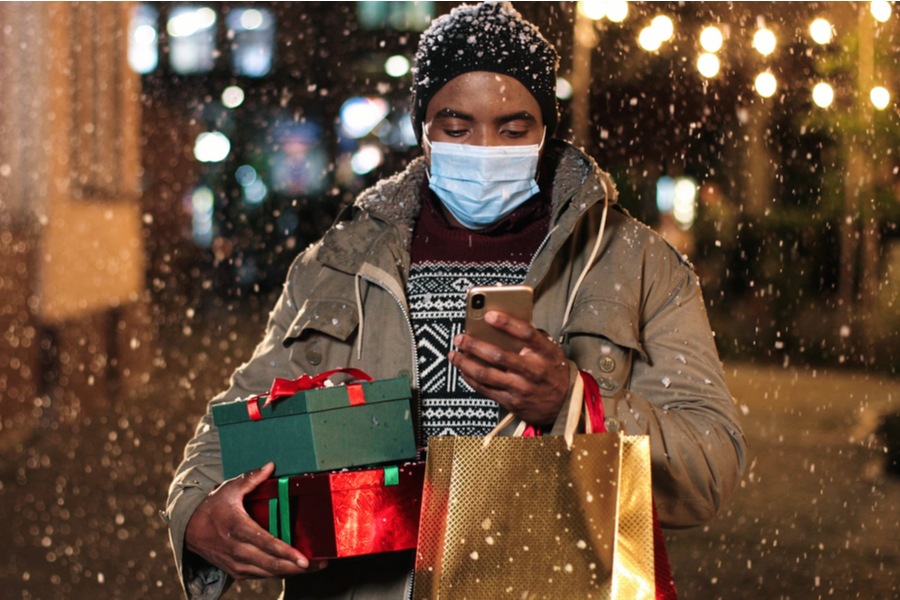 African-american man holding holiday packages and wearing a face covering